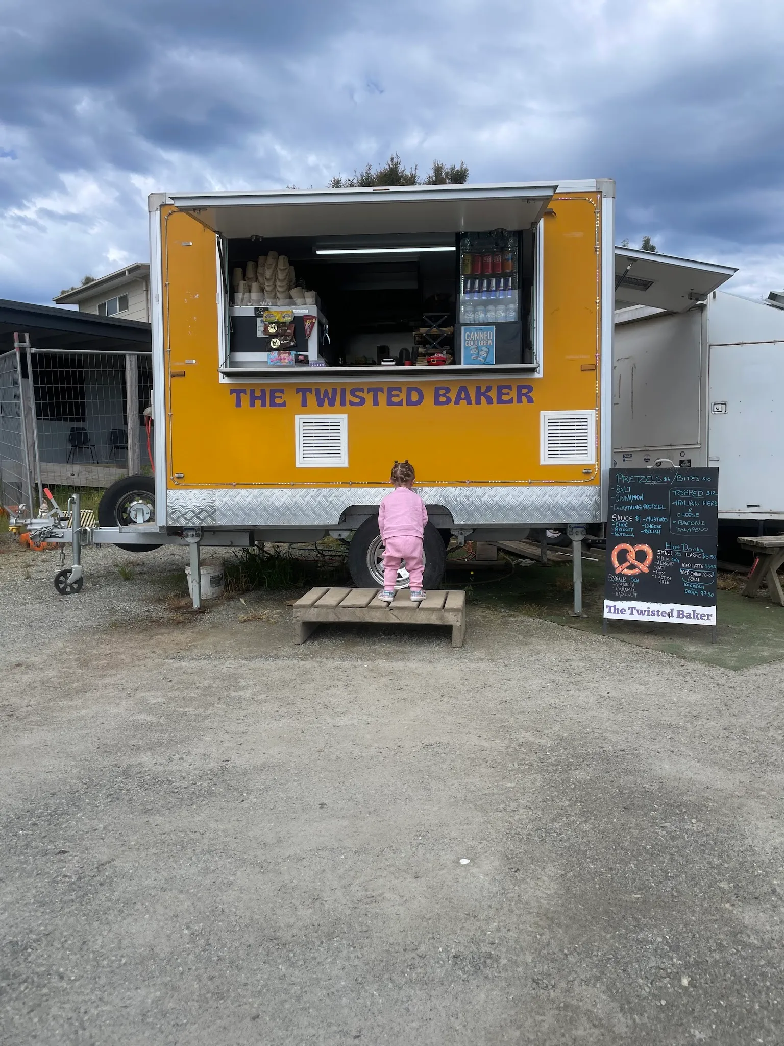 The Twisted Baker yellow food truck from behind with a child at the service window