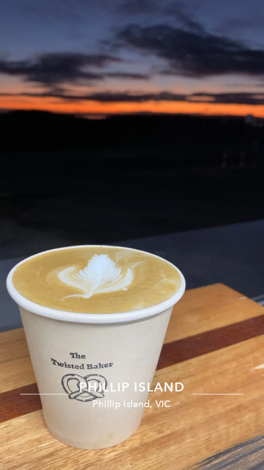 The Twisted Baker branded coffee cup with latte art against a Phillip Island sunset sky